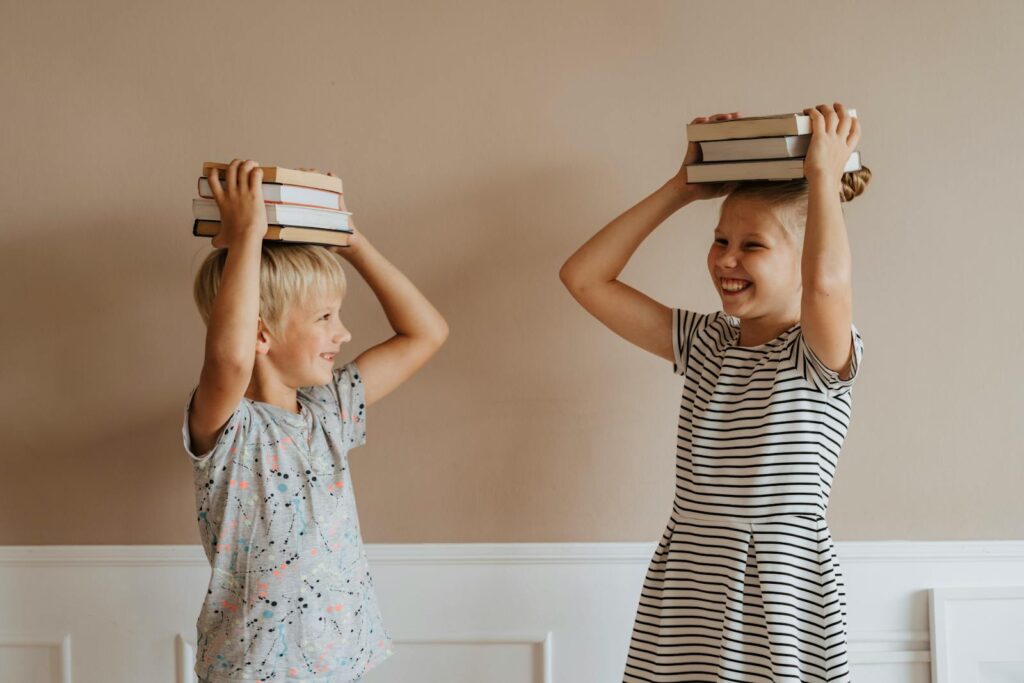Two smiling children balancing books on their heads indoors, symbolizing fun in learning english.